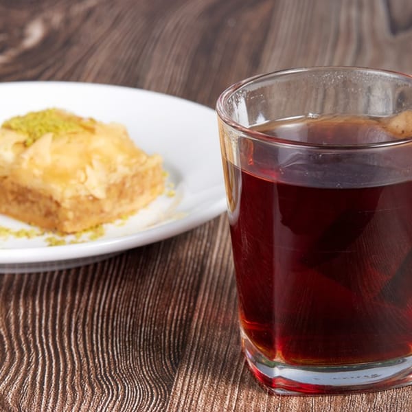 A glass of hot Mediterranean tea next to a piece of baklava topped with pistachios.
