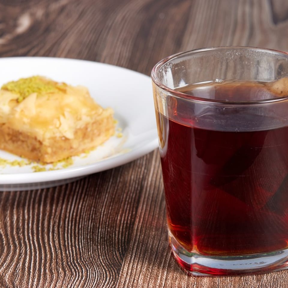 A glass of hot Mediterranean tea next to a piece of baklava topped with pistachios.