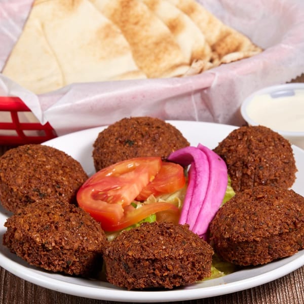 A plate of falafel with sliced tomatoes, lettuce, pink pickled vegetables, and pita bread.