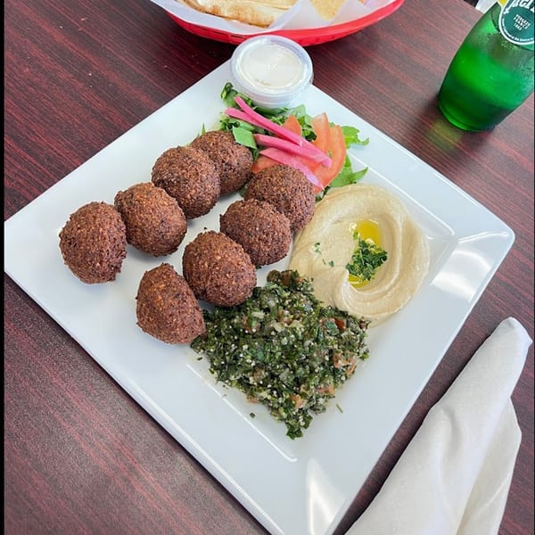 A Mediterranean falafel platter with hummus, tabbouleh, pickled vegetables, and a side of pita bread.