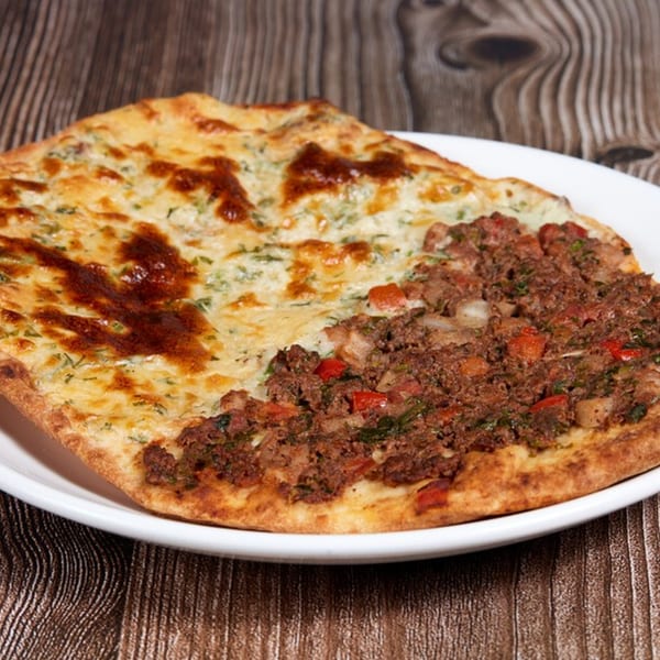 A Mediterranean flatbread, half topped with melted cheese and herbs, and half with seasoned ground meat.