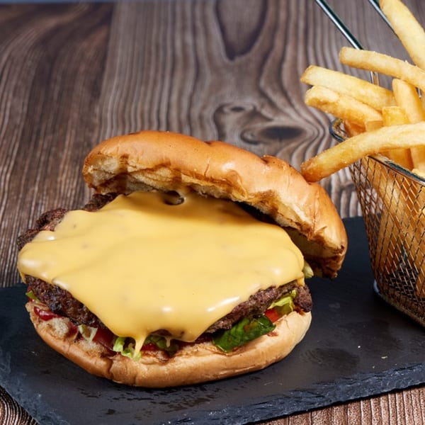 A cheeseburger with melted cheese, lettuce, and tomato, served with a side of fries.